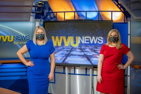 two women standing in front of a "WVU News" sign 